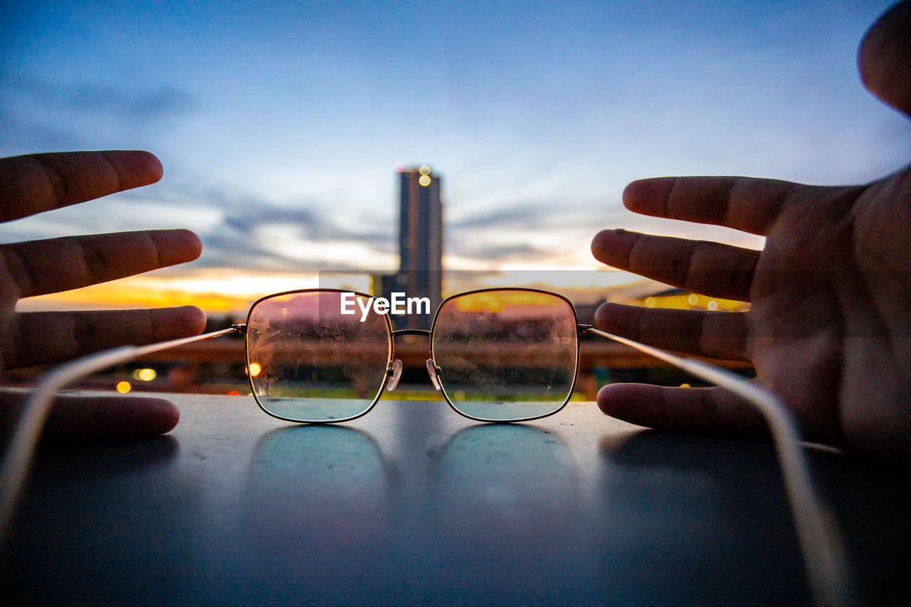 Close-up of hand holding eyeglasses against sky