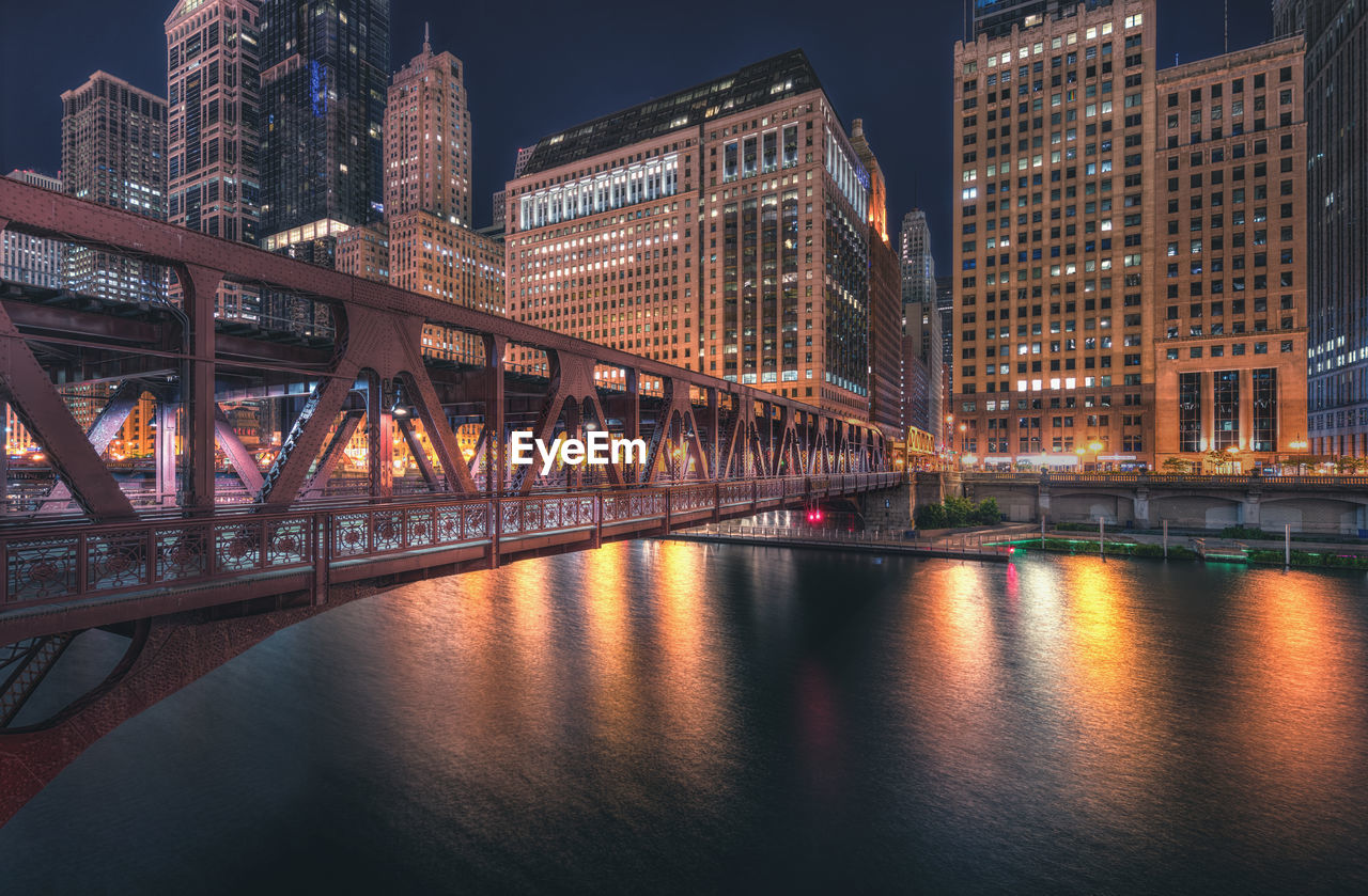 Illuminated bridge over river by buildings in city at night