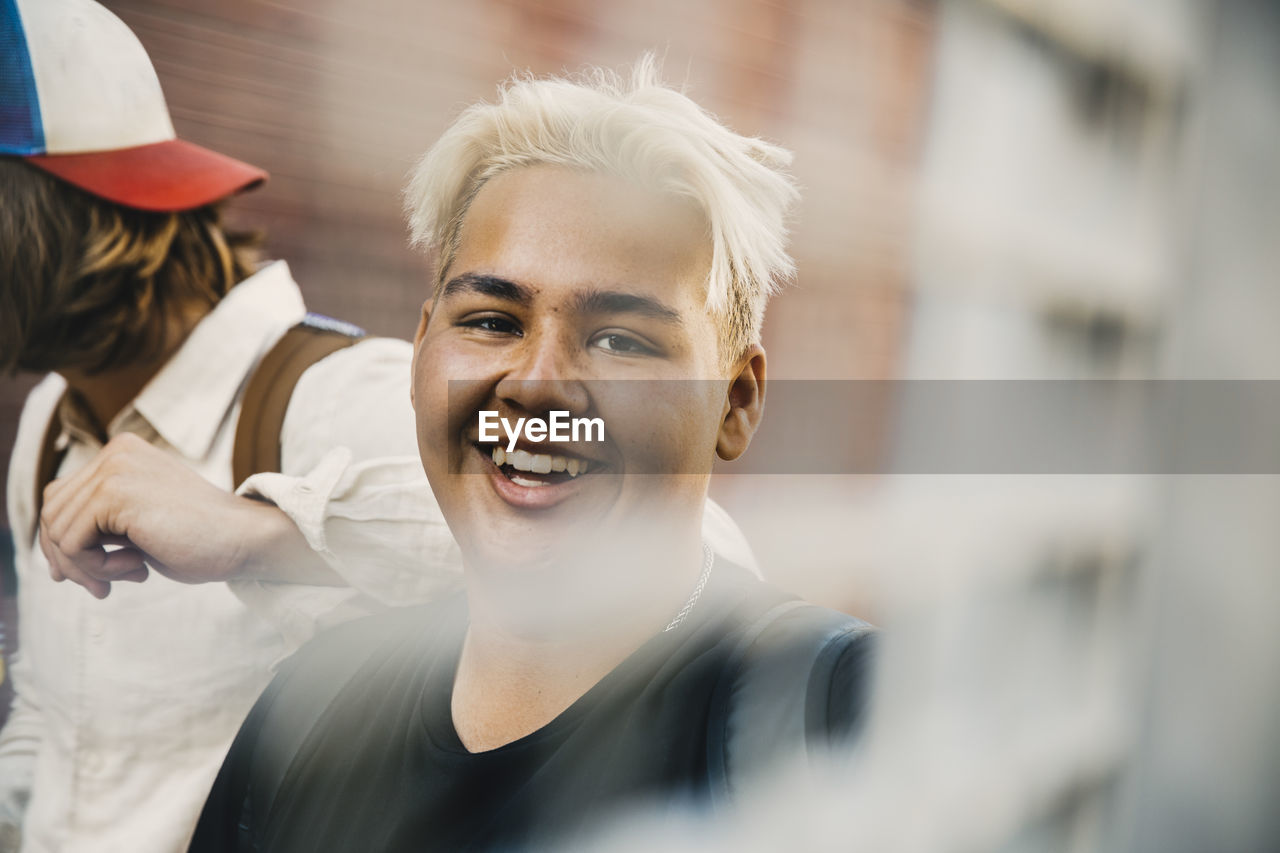 Portrait of smiling teenager with friend standing in city