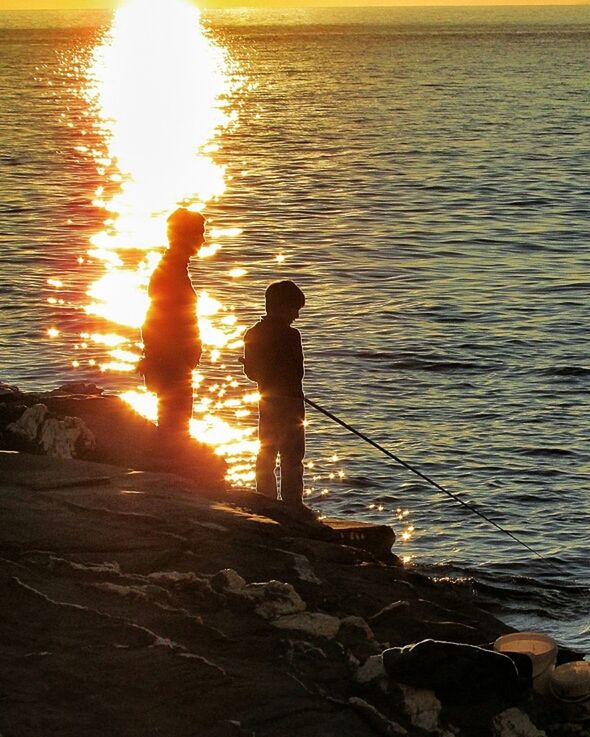 Silhouette boy fishing in calm sea at sunset