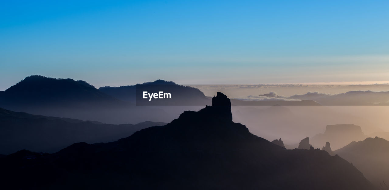 Scenic view of silhouette mountains against clear blue sky during sunset