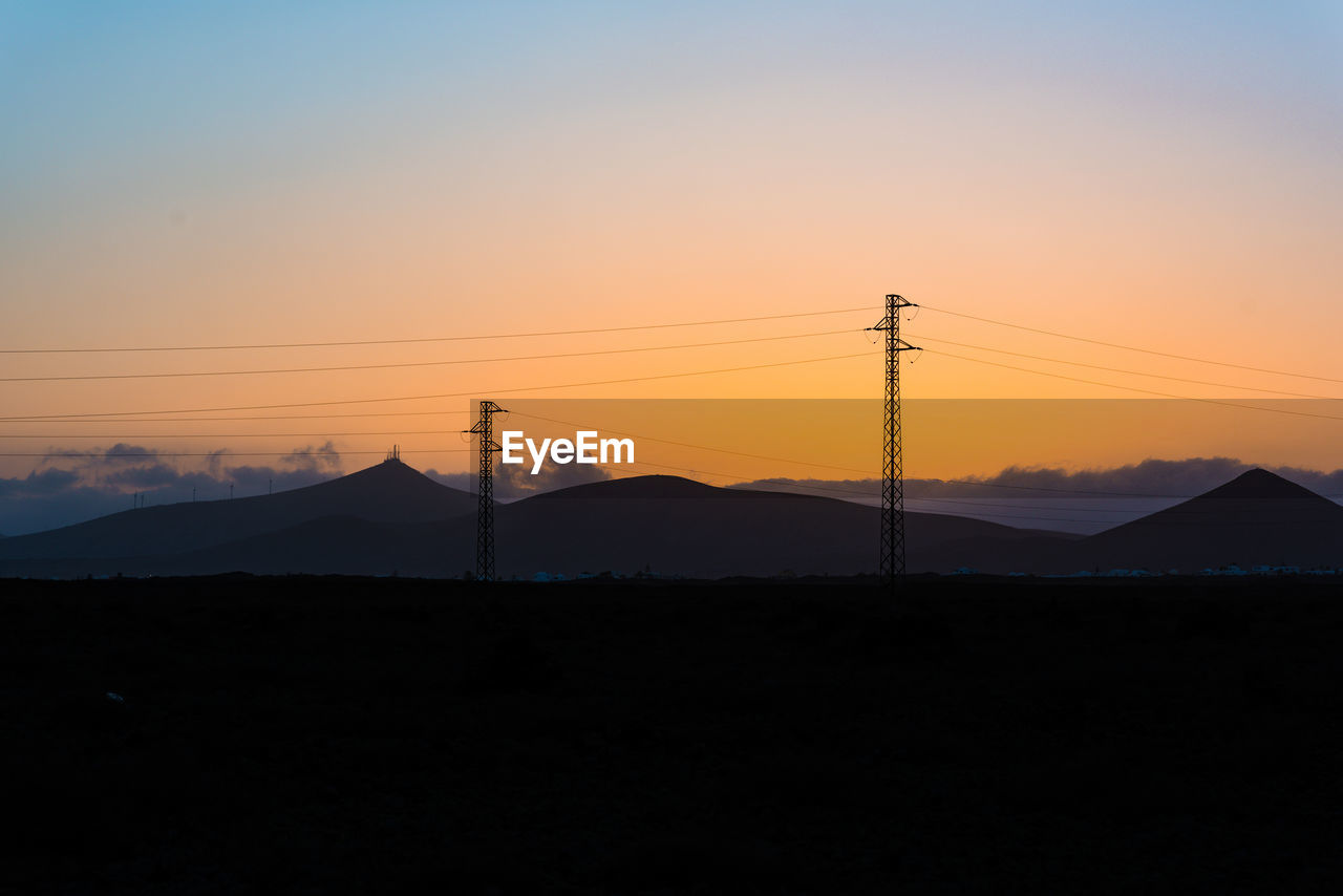 Silhouette electric pylons against sky during sunset