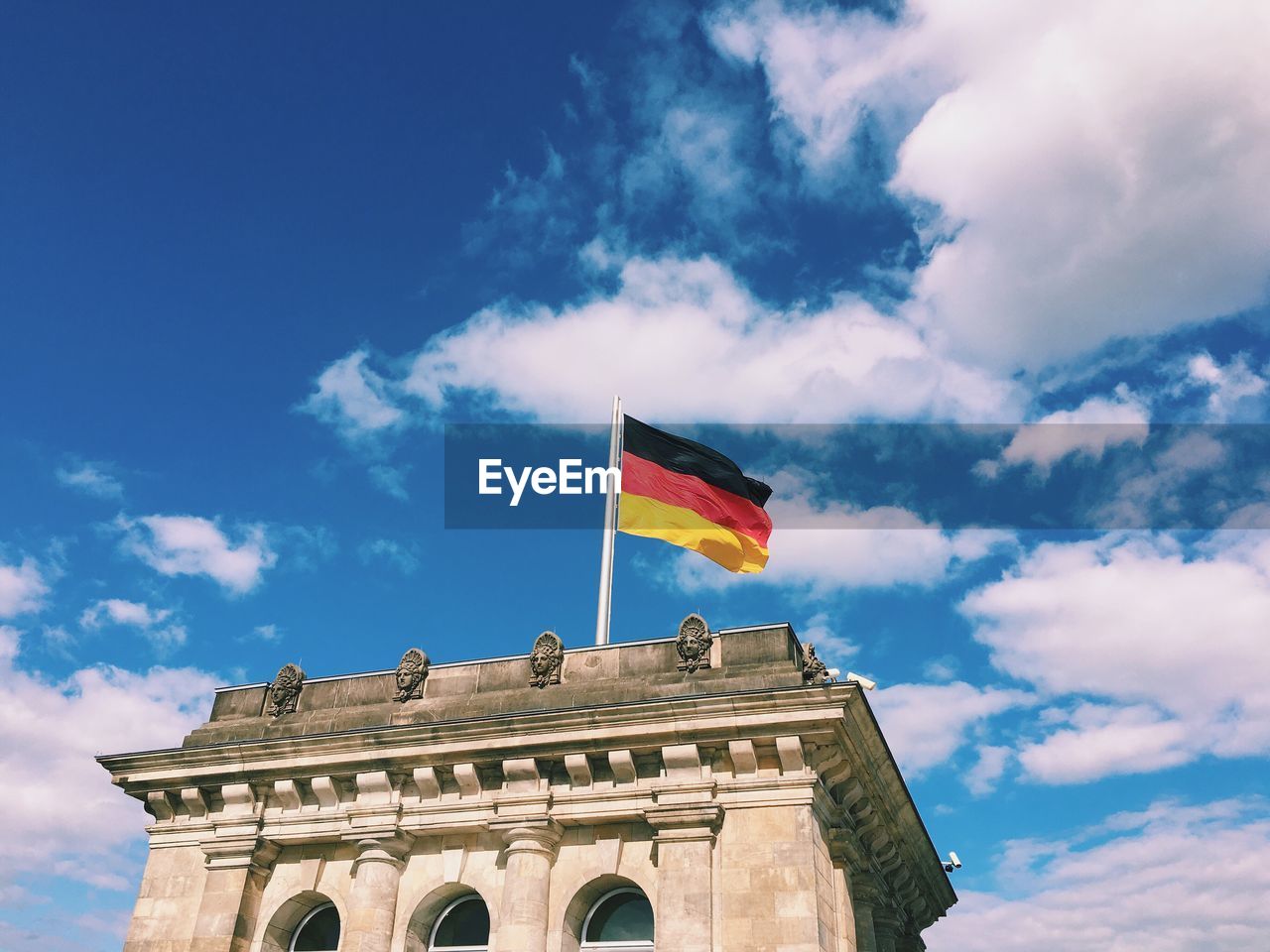 Low angle view of german flag on the reichstag against cloudy blue sky during sunny day