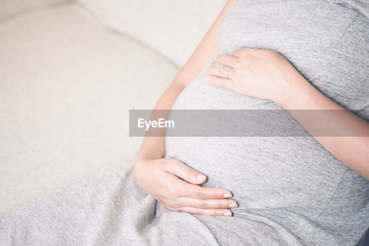 Midsection of pregnant woman sitting on sofa at home