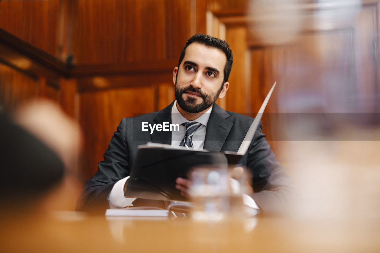 Confident bearded male financial advisor with contract file sitting in board room during meeting