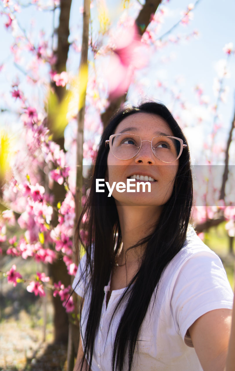 Portrait of a woman with glasses walking through a field of flowering peach trees in aitona
