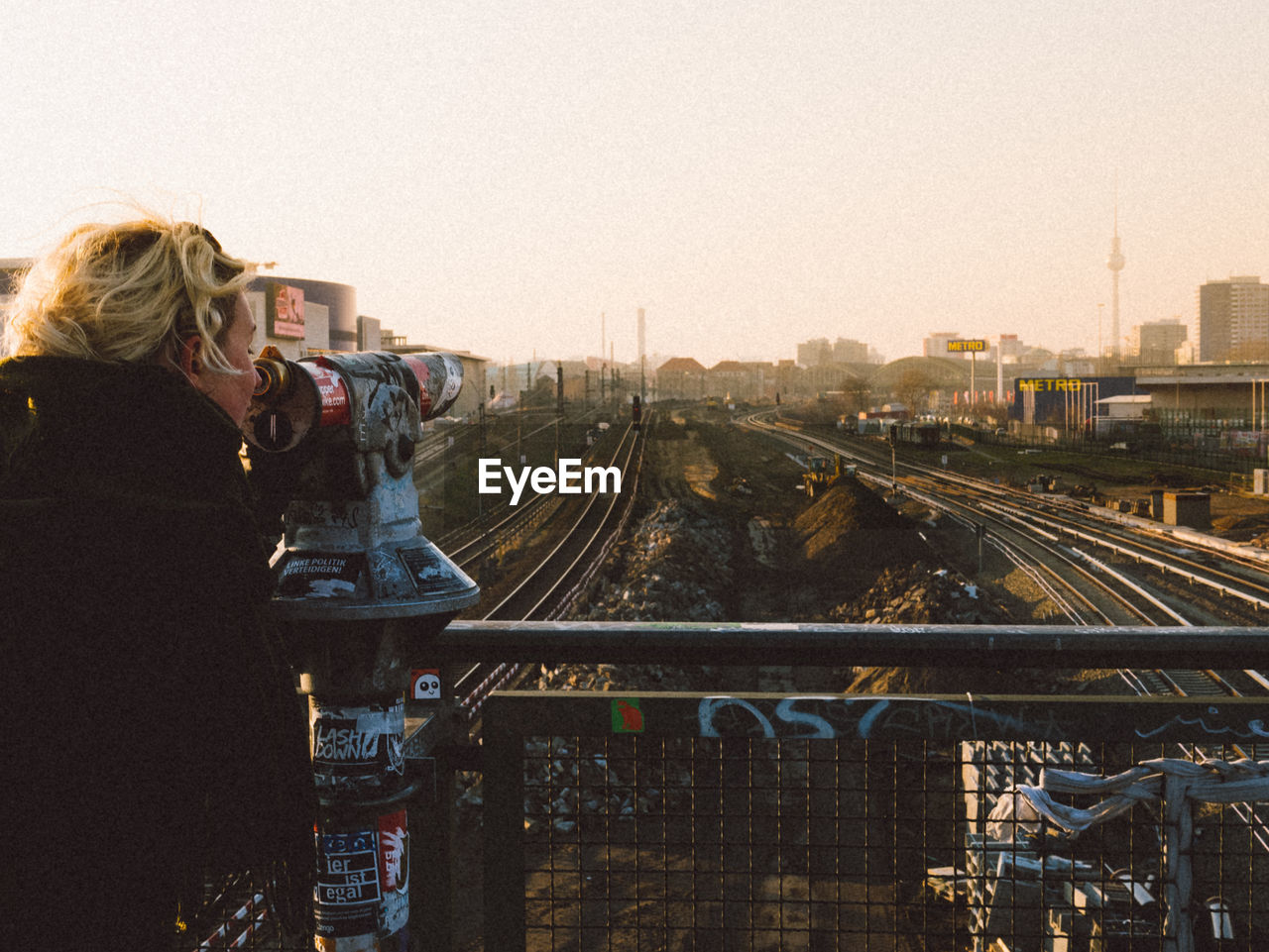 Side view of woman looking in coin-operated binoculars at railroad tracks