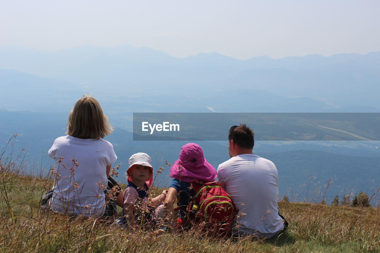 Family sitting on mountain against sky