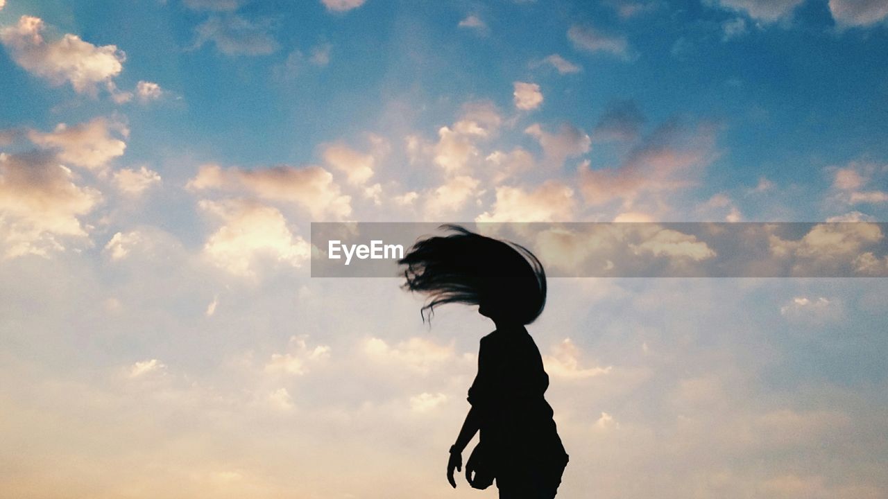Silhouette woman tossing hair against cloudy sky during sunrise