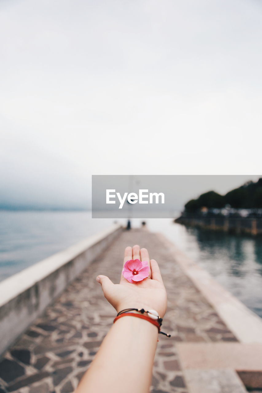 Midsection of person with hand against sea against sky