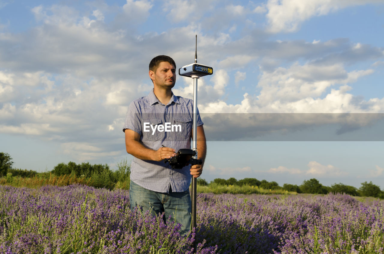 Surveyor using equipment on lavender field against cloudy sky