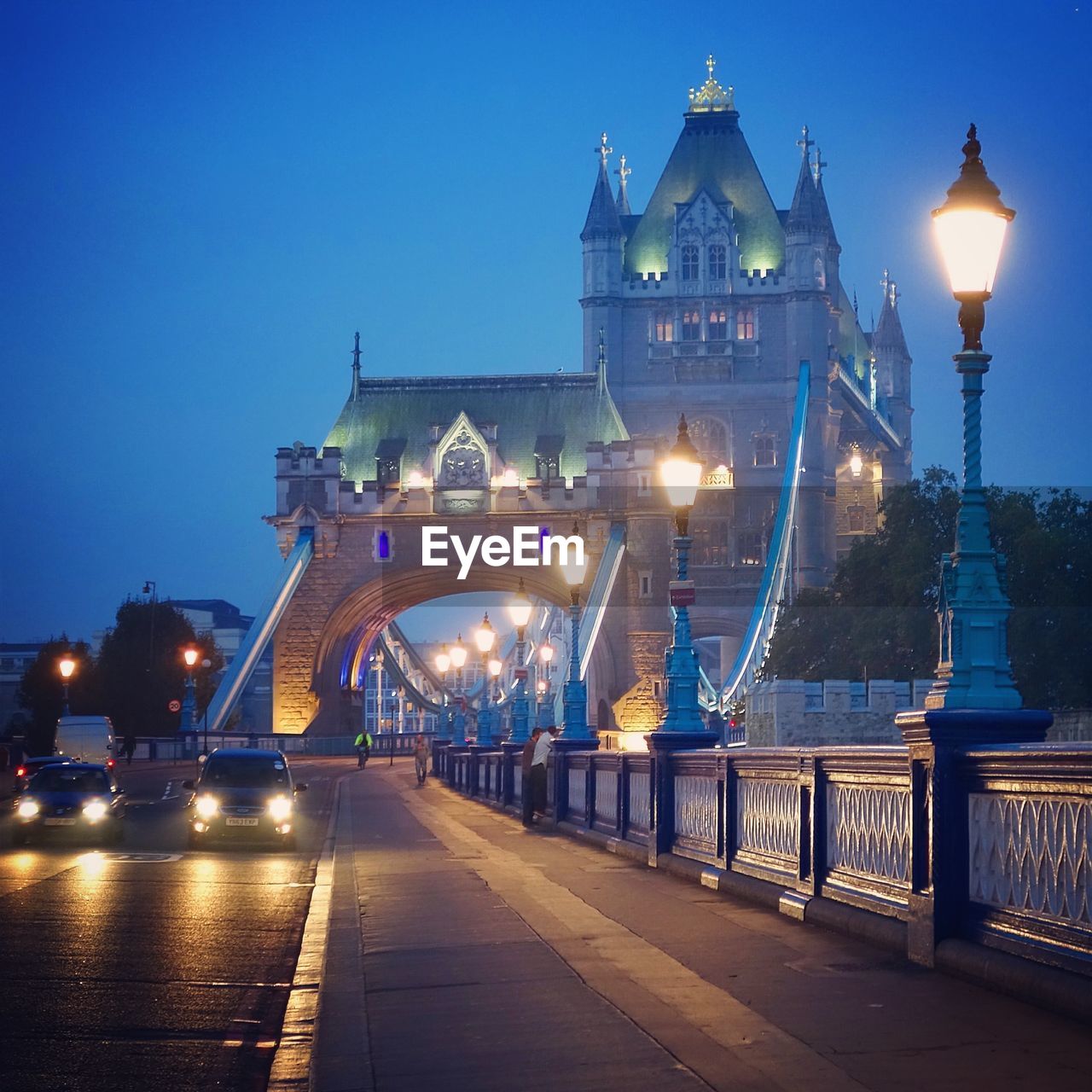 Cars on illuminated tower bridge in city at dusk