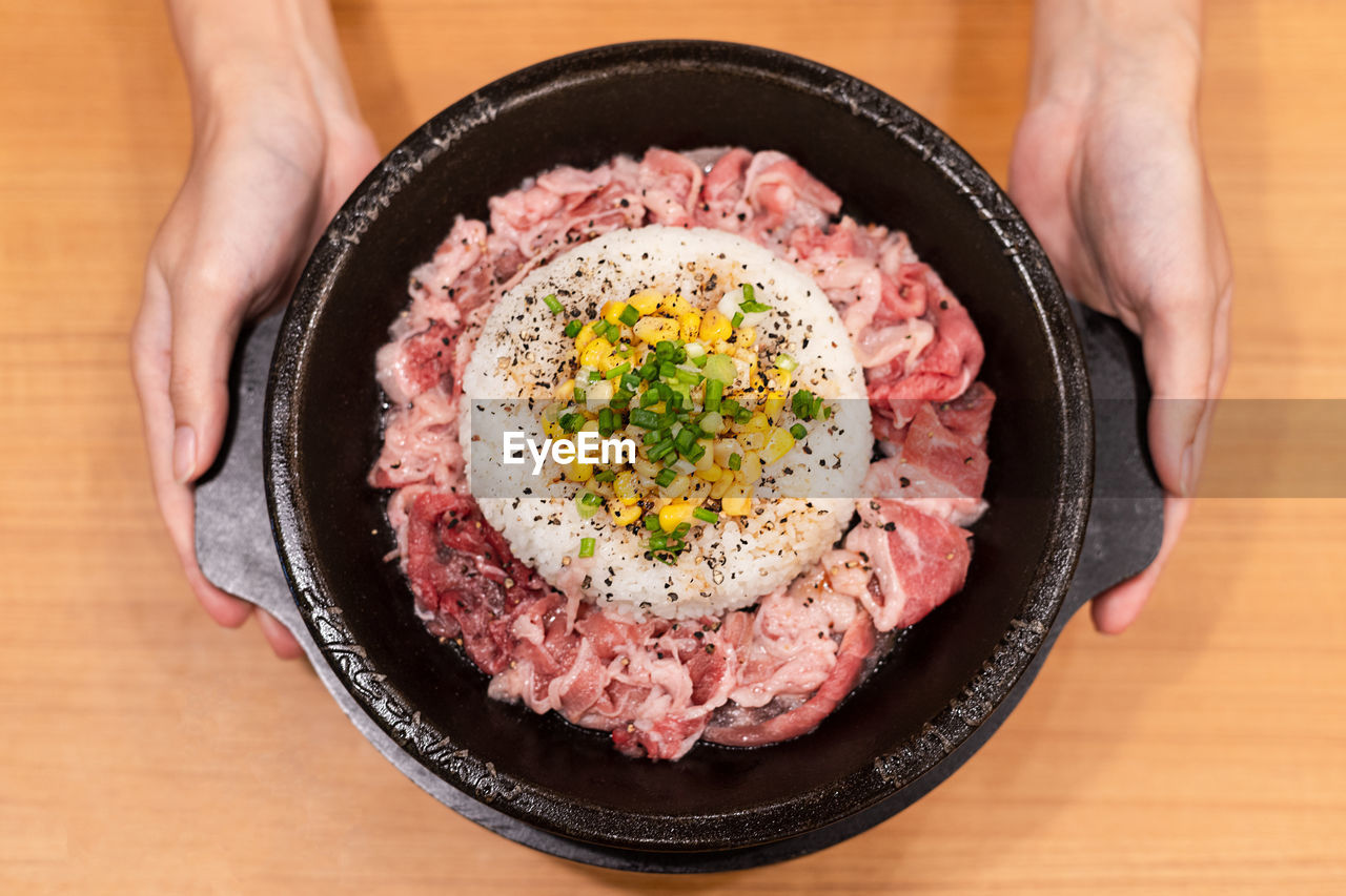 Raw meat with rice have vegetable on top put on hot plate prepare to cook, with two hand holding