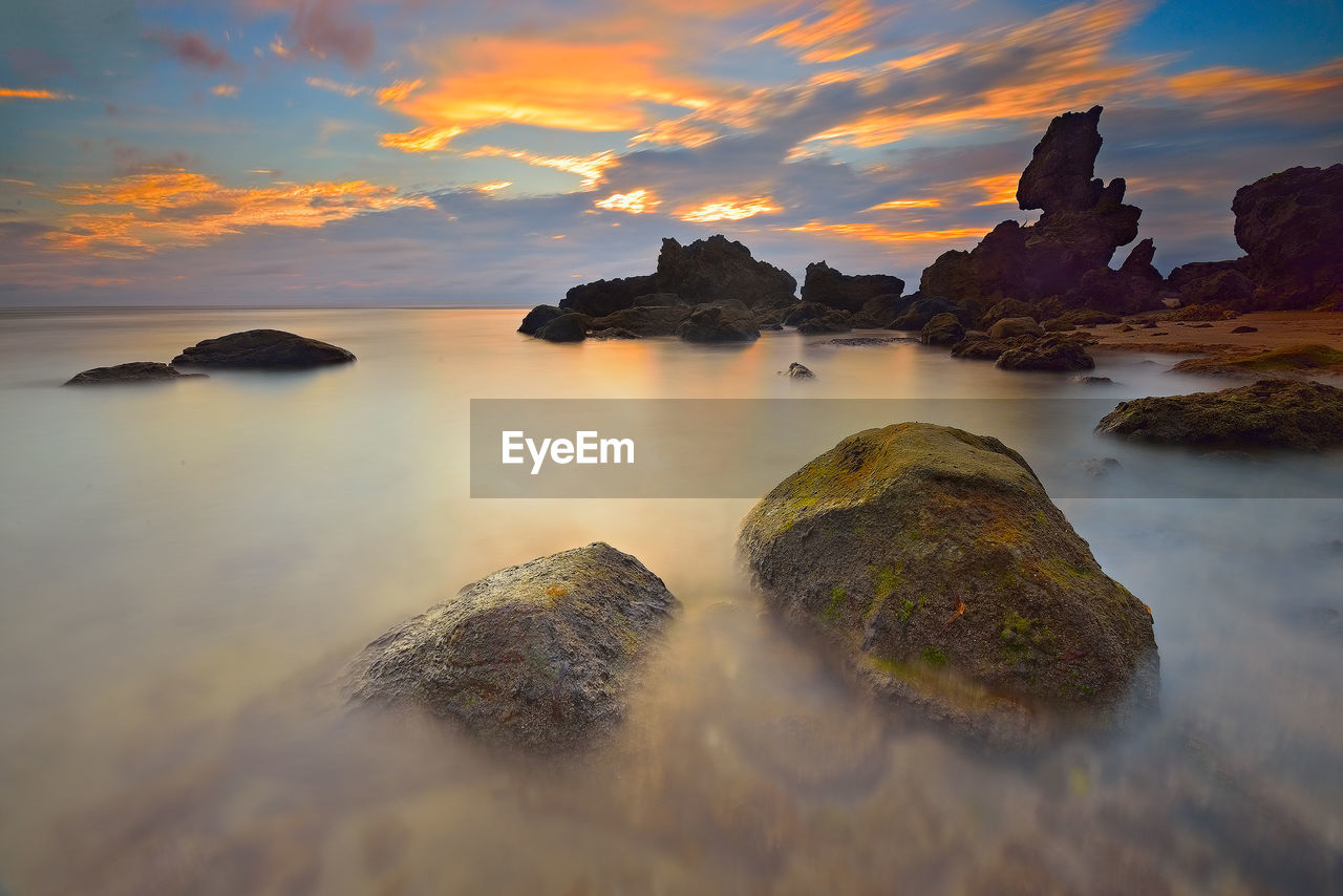 Scenic view of sea and rock formation against sky during sunset