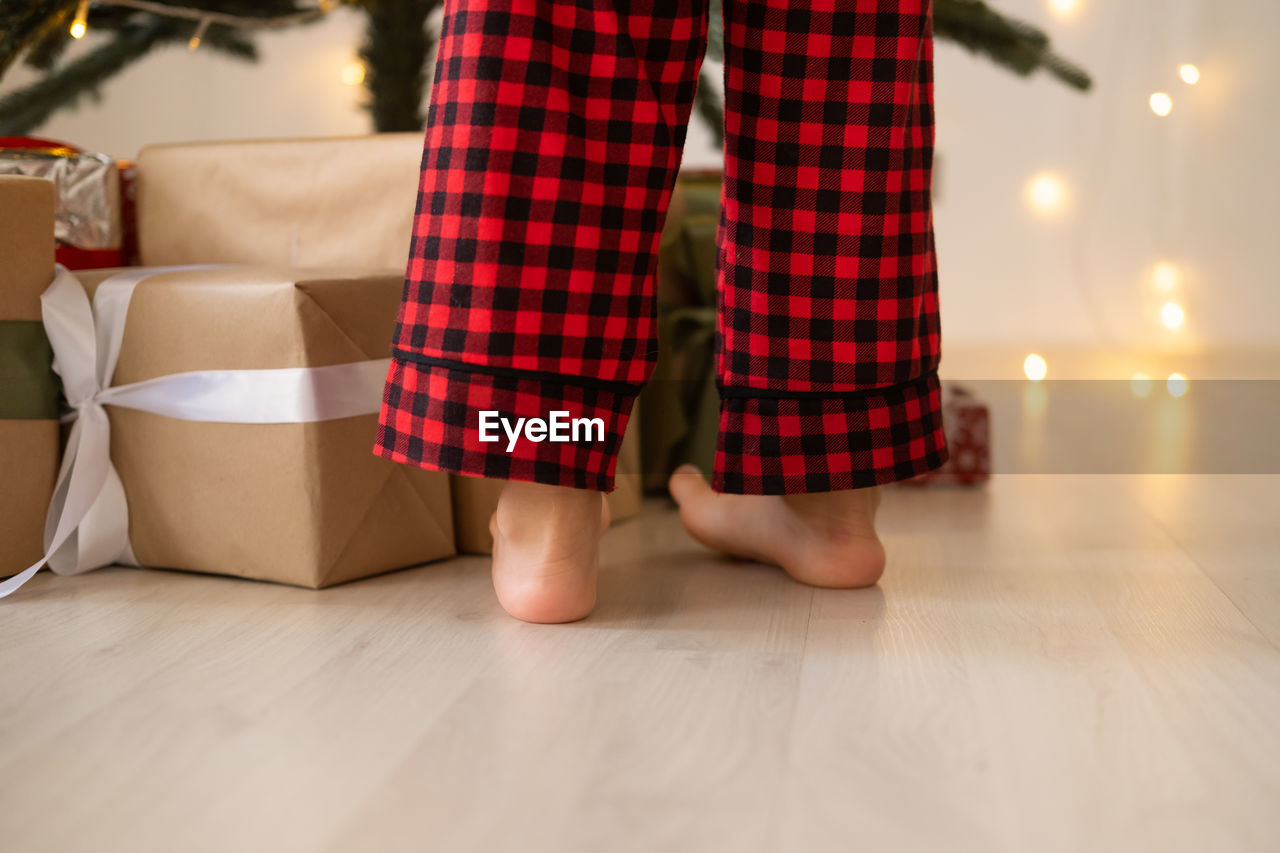 Close up kid legs in red christmas pajama near gift boxes
