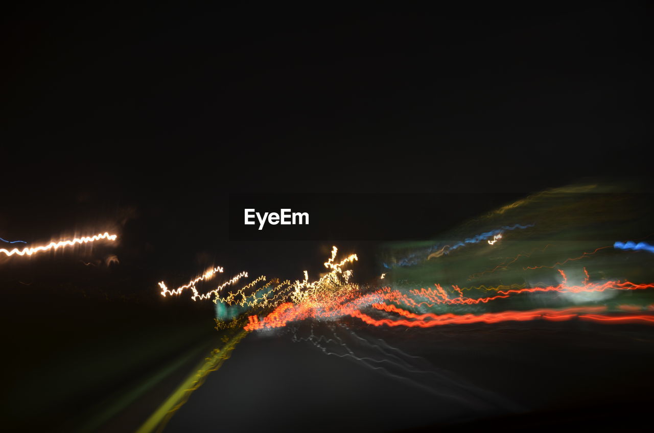 Light trails over road against clear sky at night