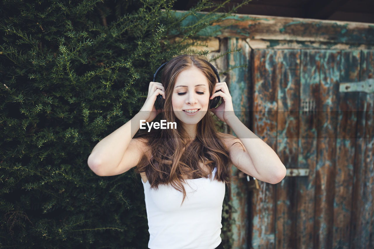 Young woman with closed eyes listening to music via headphones outdoors. spring or summer time