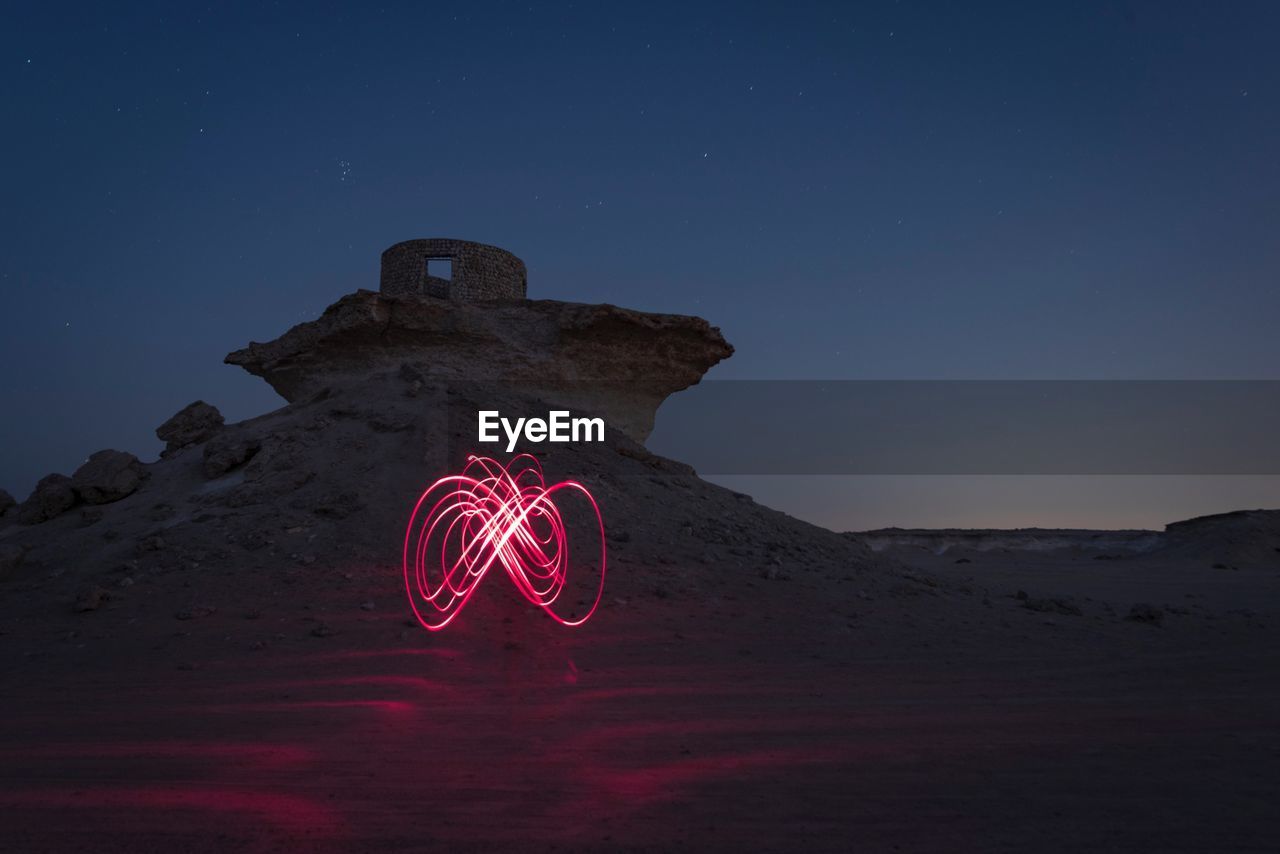 Low angle view of illuminated lighting equipment on desert against sky at night