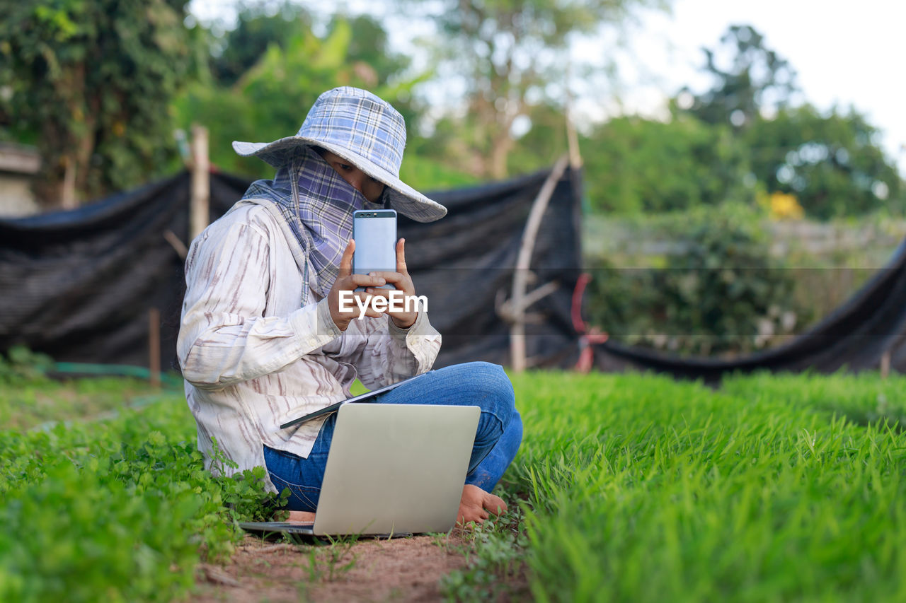 REAR VIEW OF SENIOR MAN USING MOBILE PHONE IN FIELD