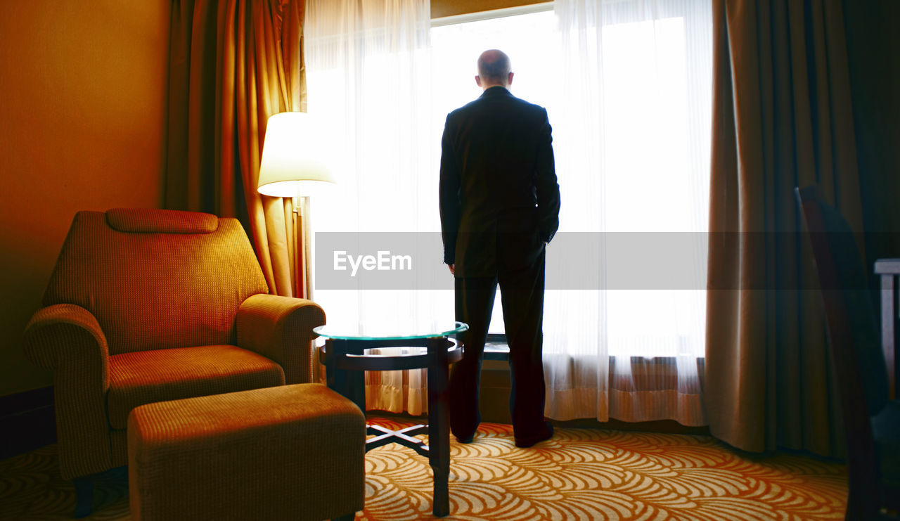 REAR VIEW OF MAN STANDING IN FRONT OF HOME