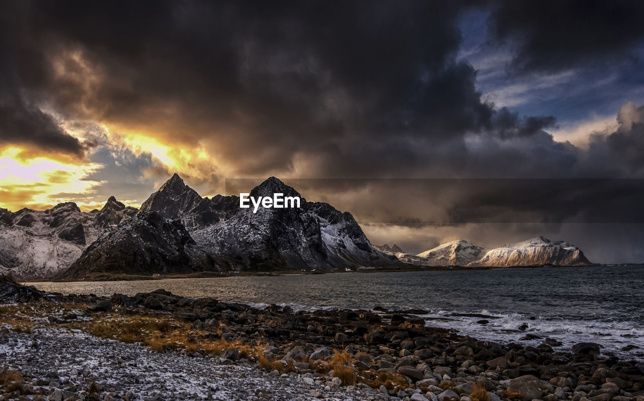 Scenic view of sea by mountains against sky during sunset