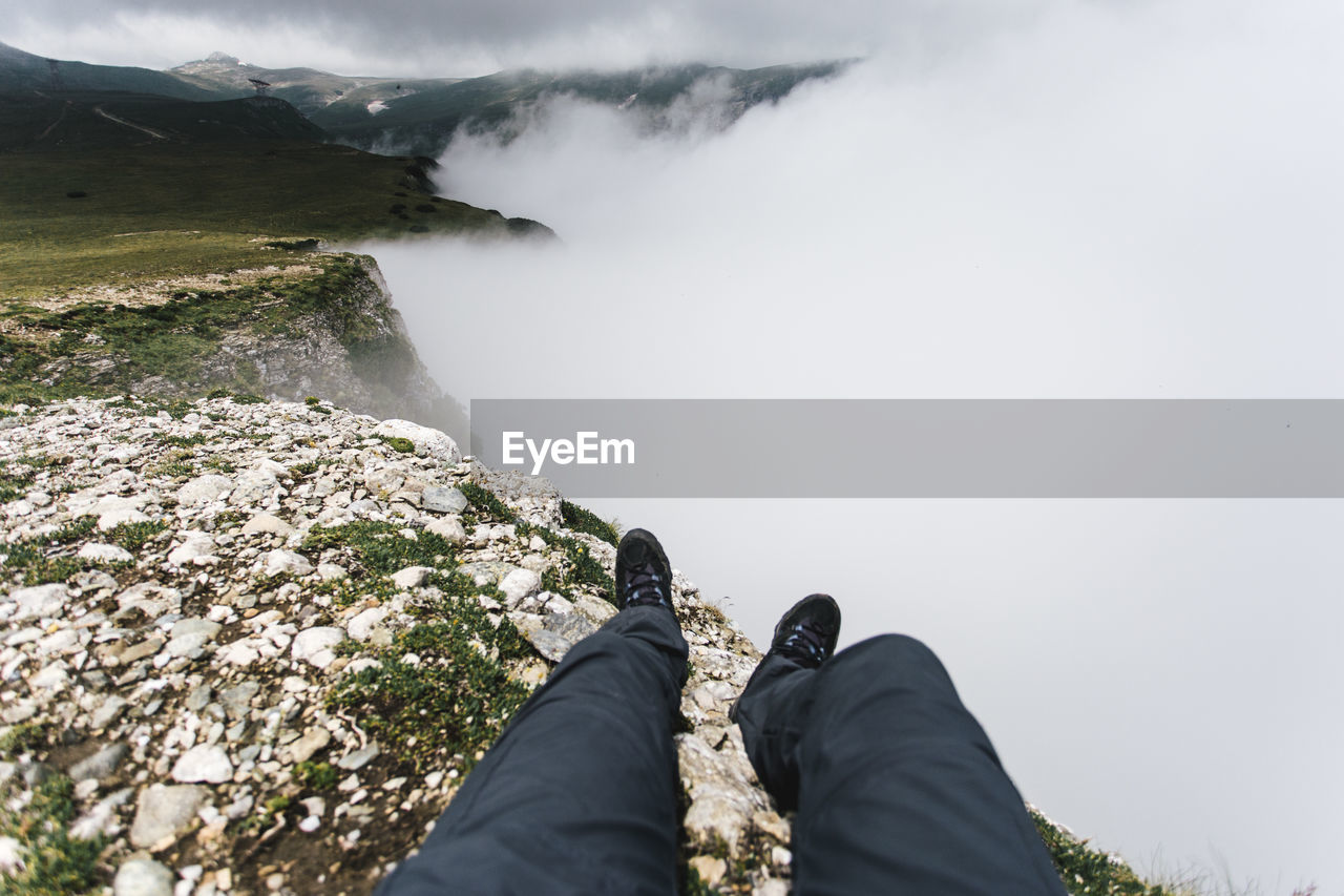Low section of man on cliff against sky during foggy weather