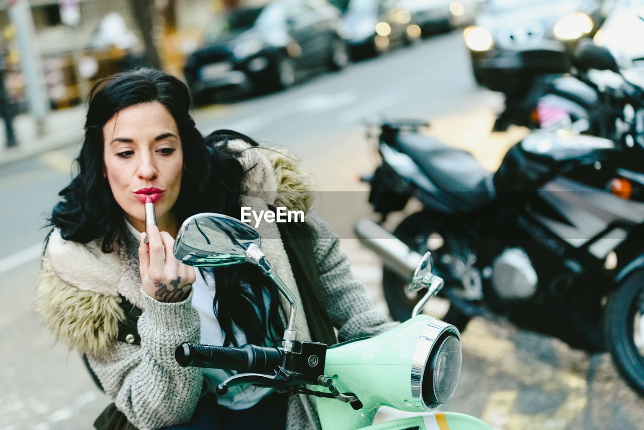 Woman applying lipstick while sitting on motor scooter