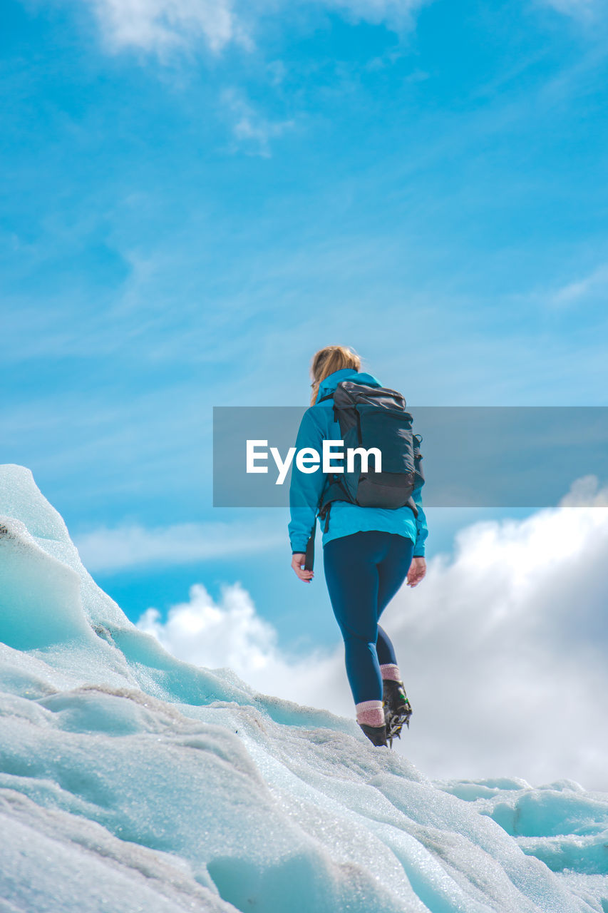 Rear view of woman walking on snow against blue sky