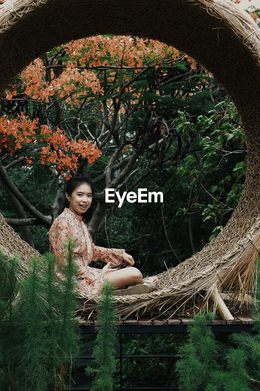 PORTRAIT OF HAPPY WOMAN SITTING ON TREE