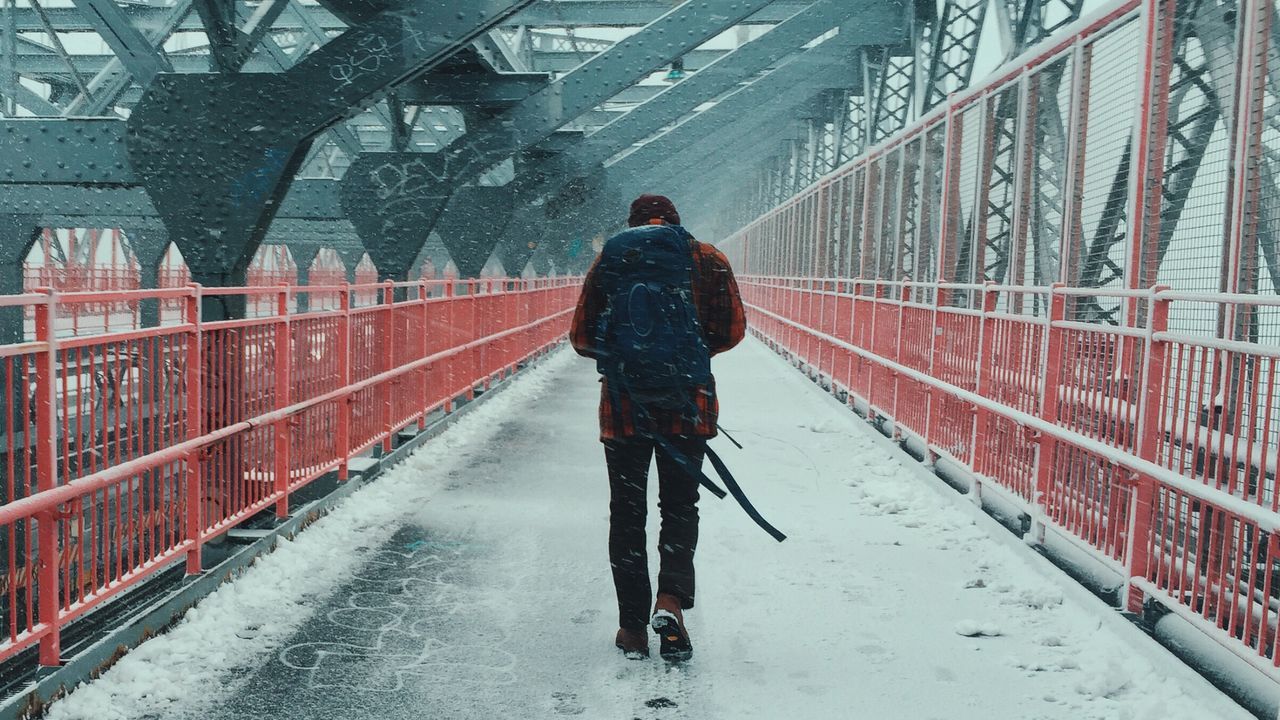 Full length rear view of man walking on bridge during snowfall