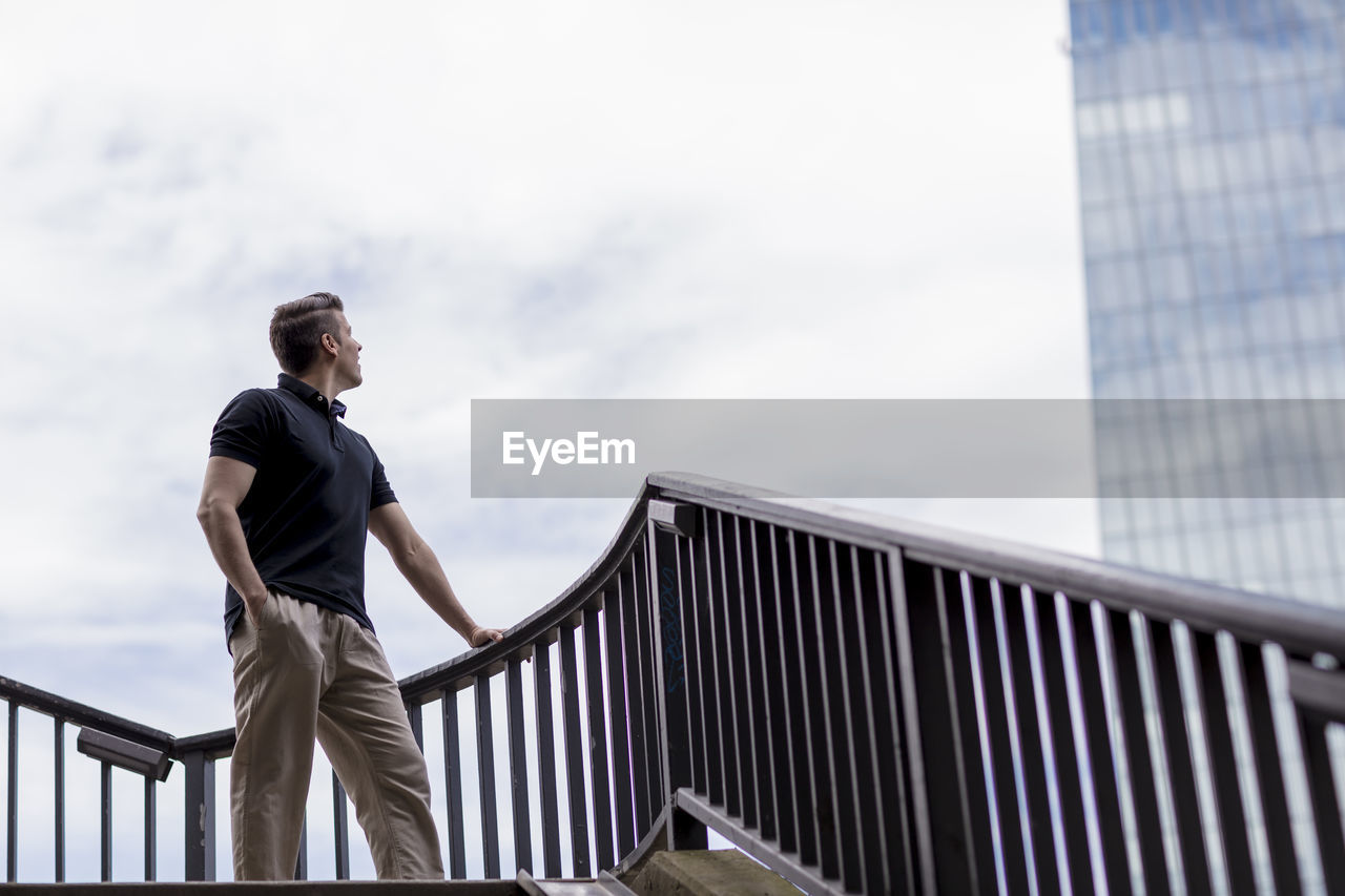 Low angle view of man looking at building against sky in city