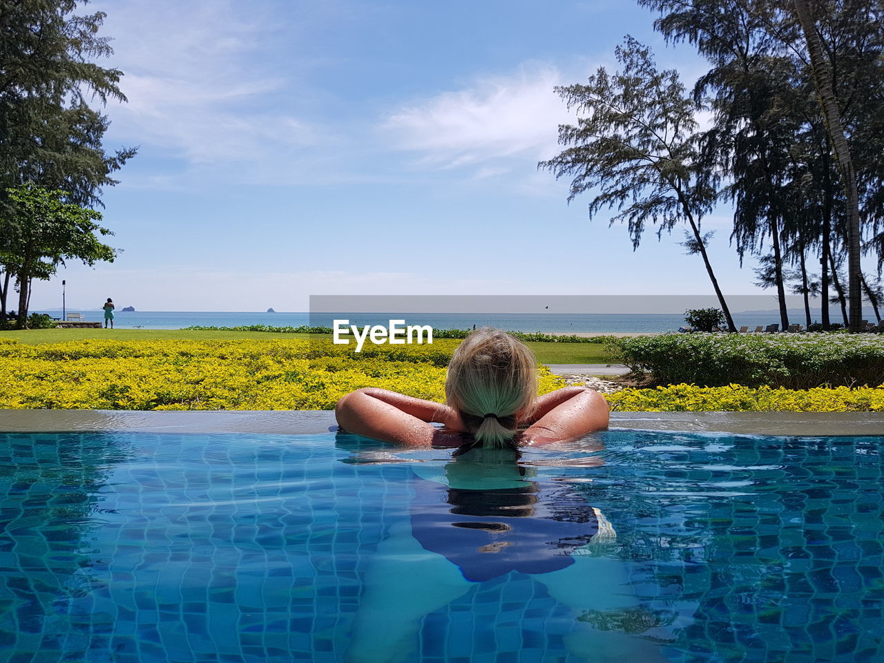 YOUNG WOMAN SWIMMING IN POOL AGAINST SEA