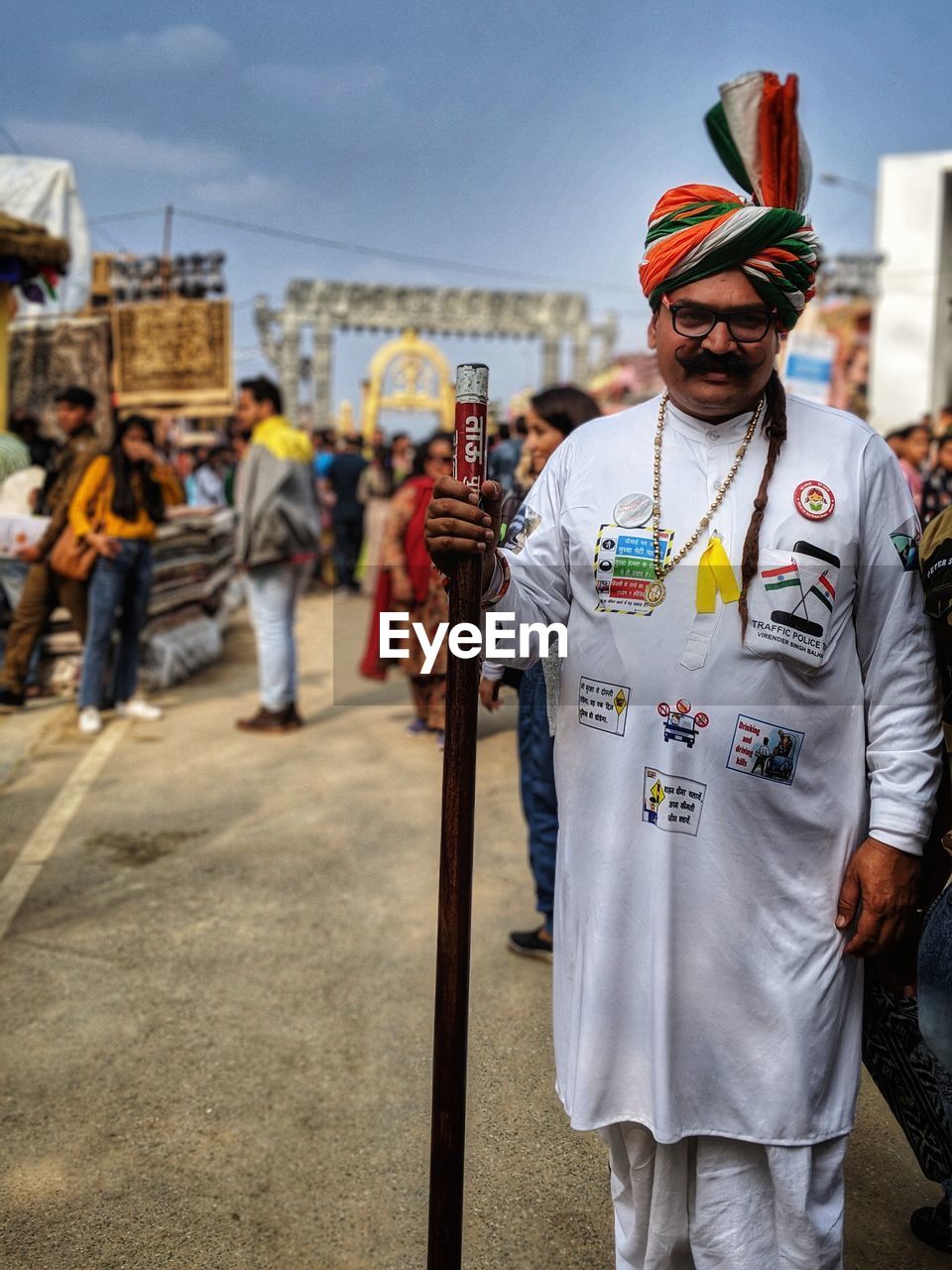 Portrait of man standing holding walking cane in traditional clothing against sky