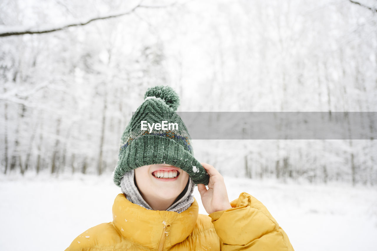 Happy boy having fun covering face with knit hat at park