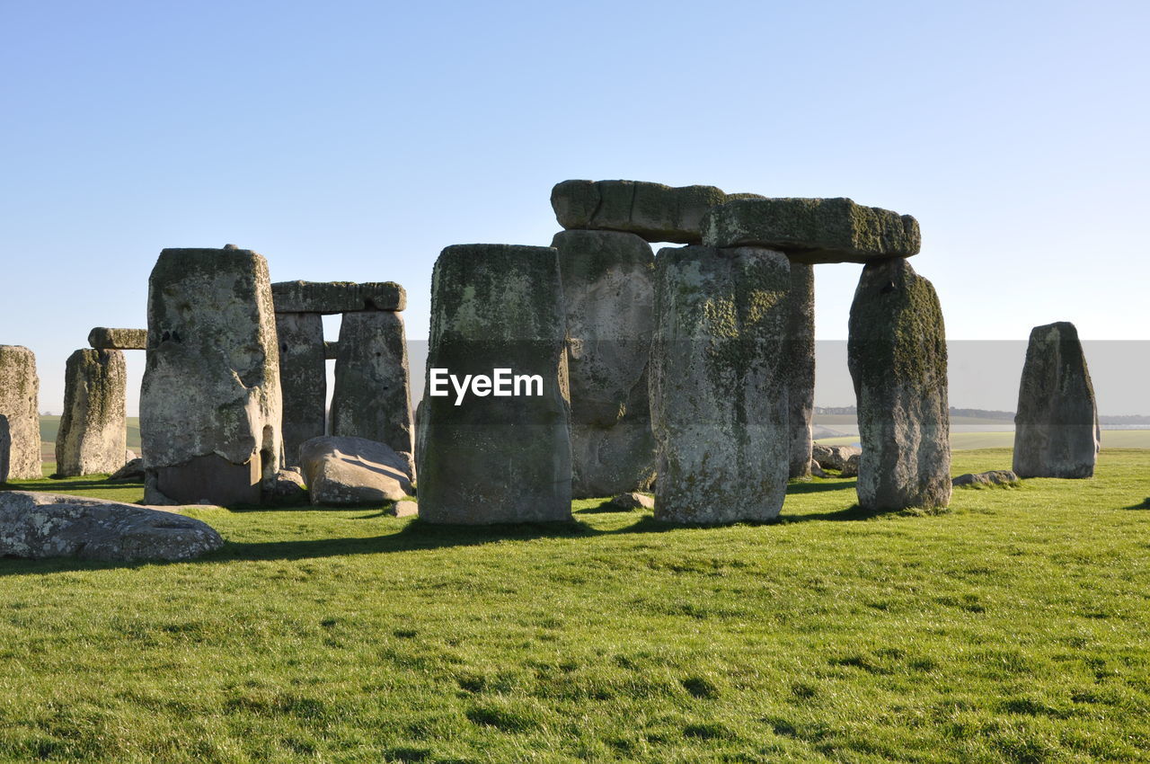Historic stonehenge on grassy field against clear sky