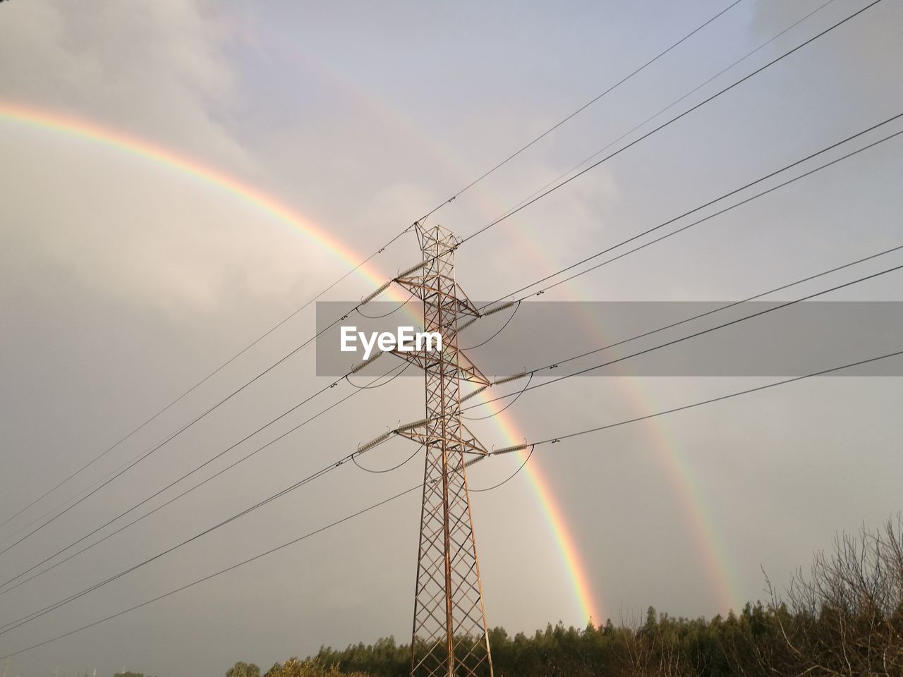 LOW ANGLE VIEW OF ELECTRICITY PYLONS AGAINST RAINBOW