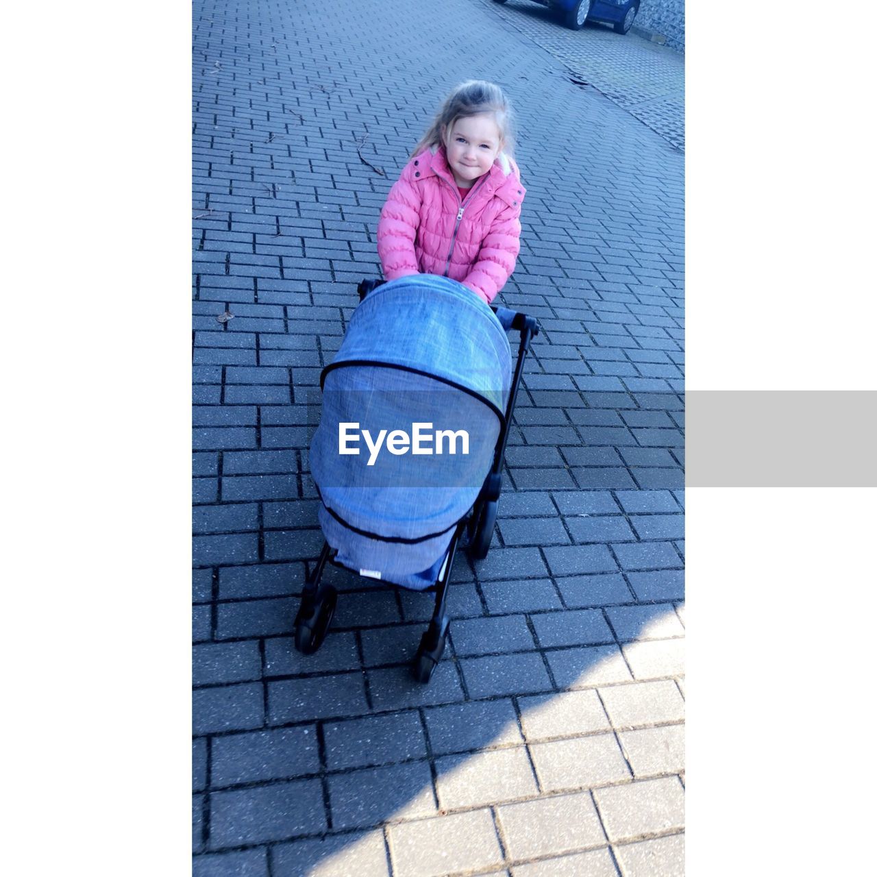 Portrait of girl pushing baby stroller on footpath