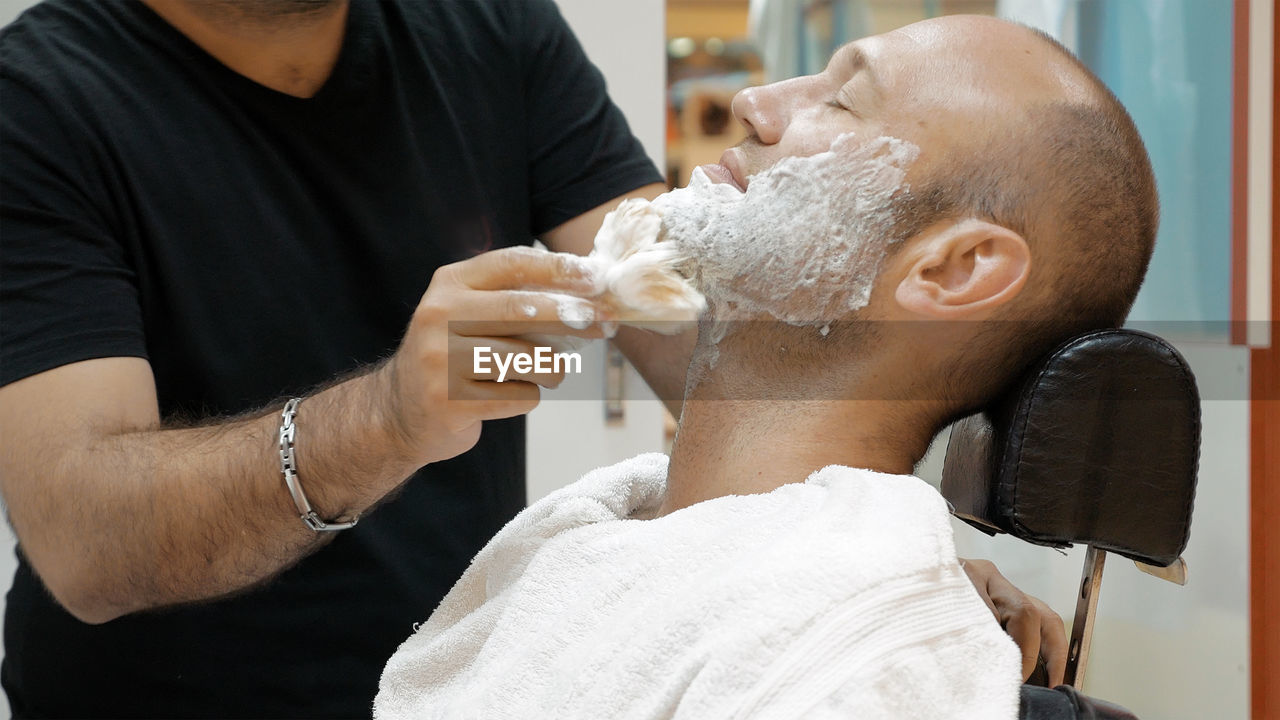 Barber applying shaving cream on mature man in salon