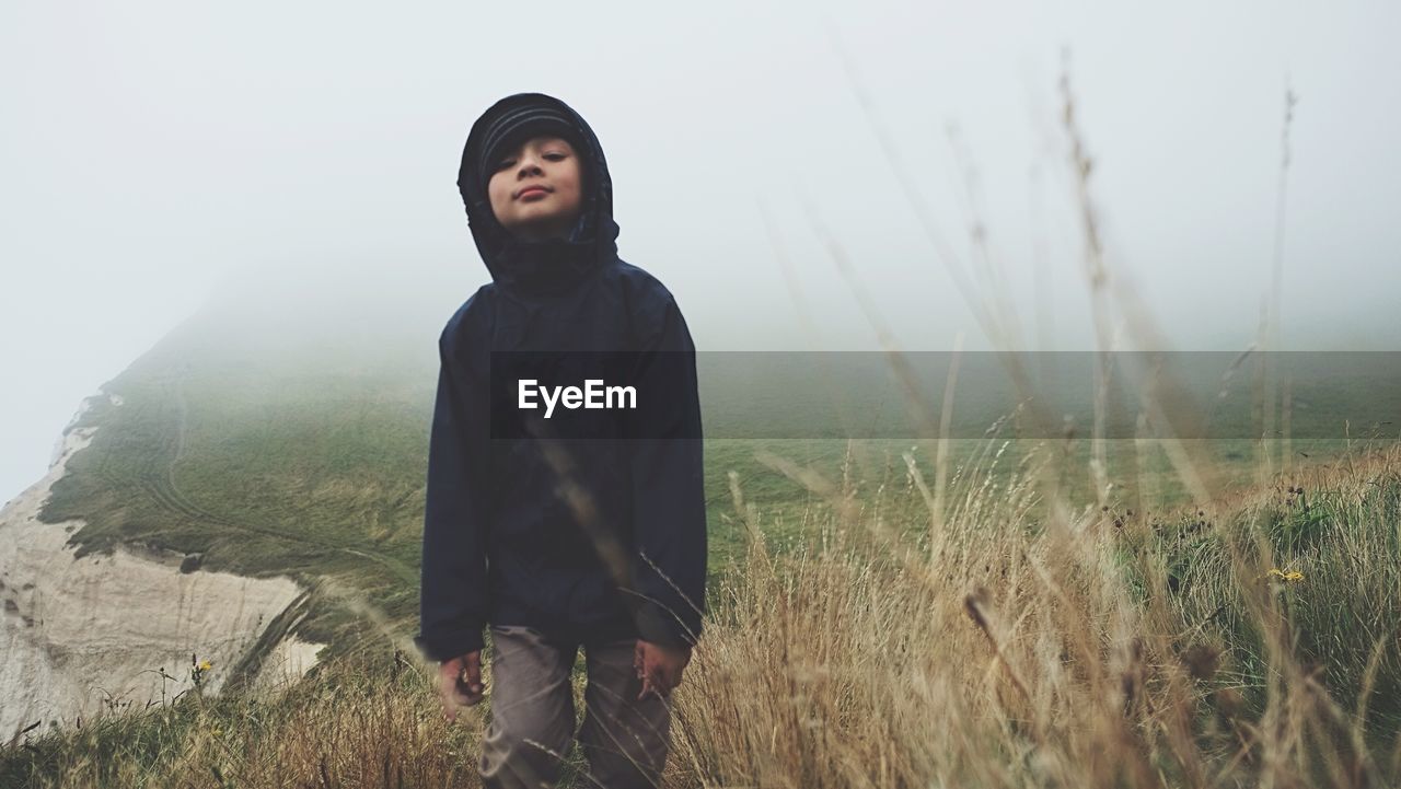 Young boy standing on clifftop against sky