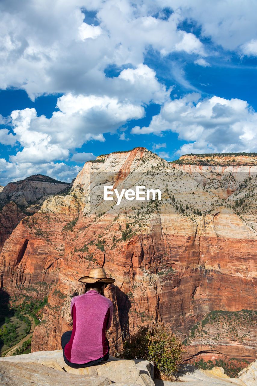 Rear view of woman sitting on rock against sky