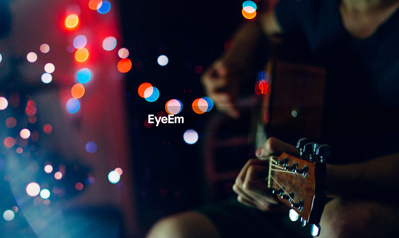 Midsection of man playing guitar by defocused lights