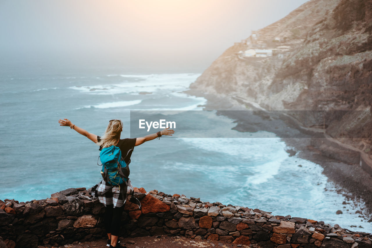 Woman with arms outstretched standing at beach against sky