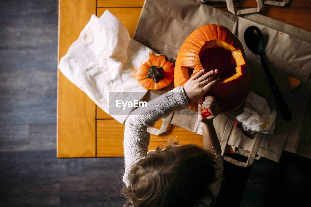 Overhead view of girl making jack o' lantern on table at home