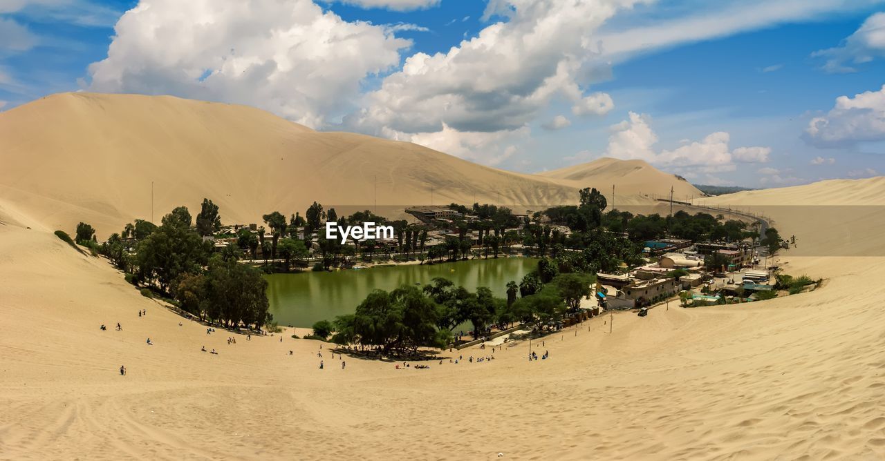 Scenic view of desert against cloudy sky during sunny day