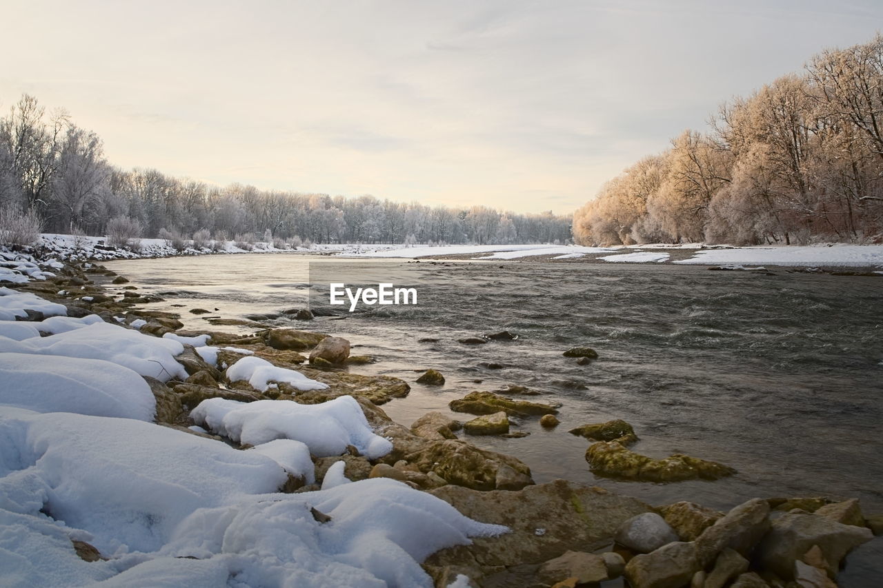 Scenic view of snow covered river bank against sky during winter
