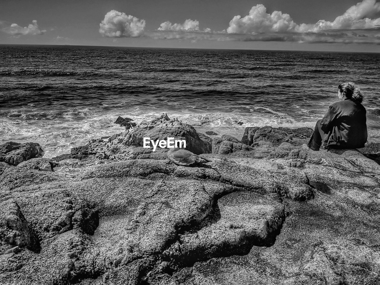 Woman sitting alone contemplating the vastness of the sea. monochrome.