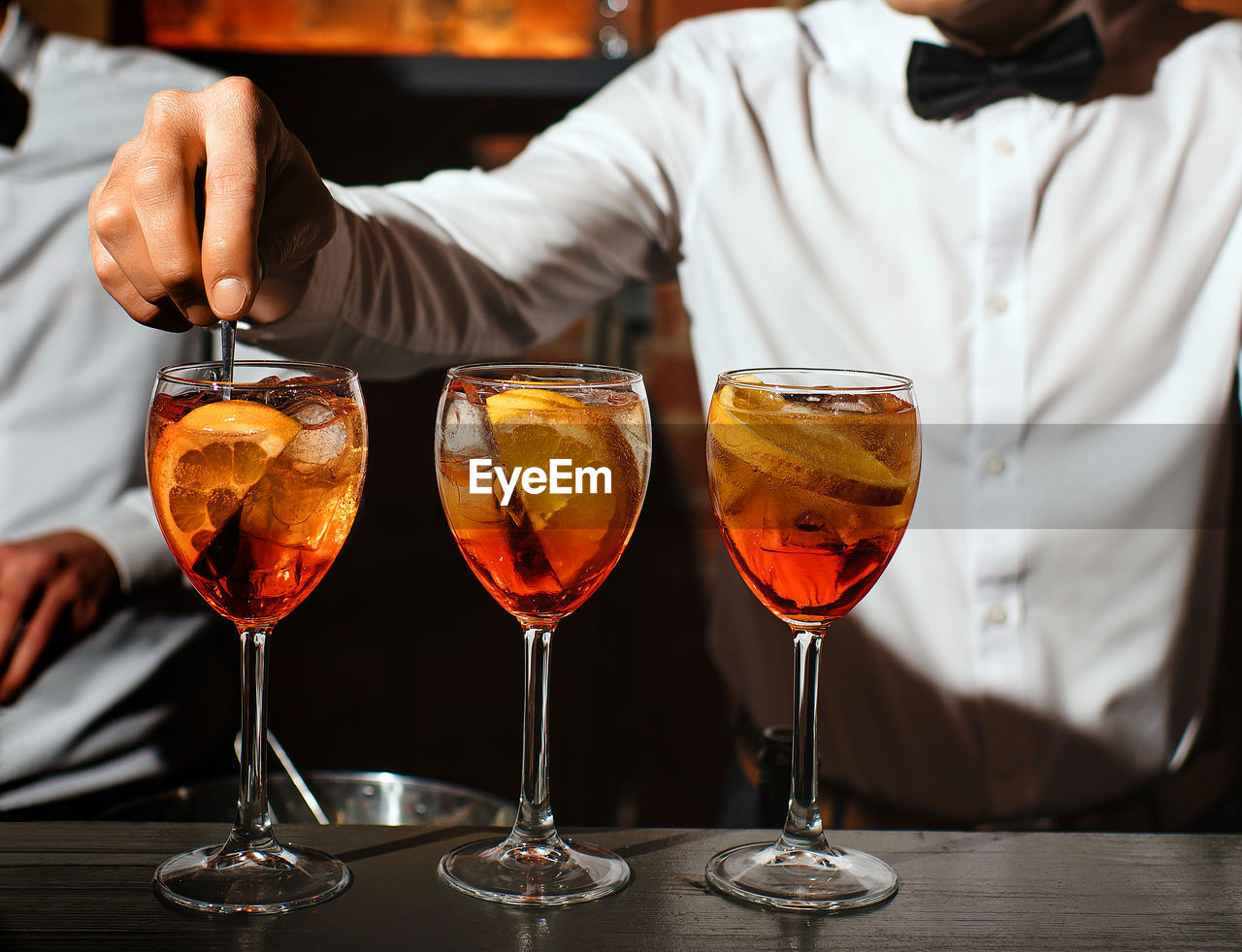 Three glass glasses with an aperol spritz cocktail are on bar bartender is stirring one of aperitifs