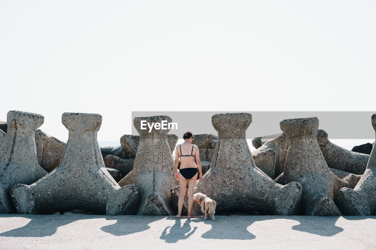 Rear view of woman standing by tetrapod rocks against clear sky