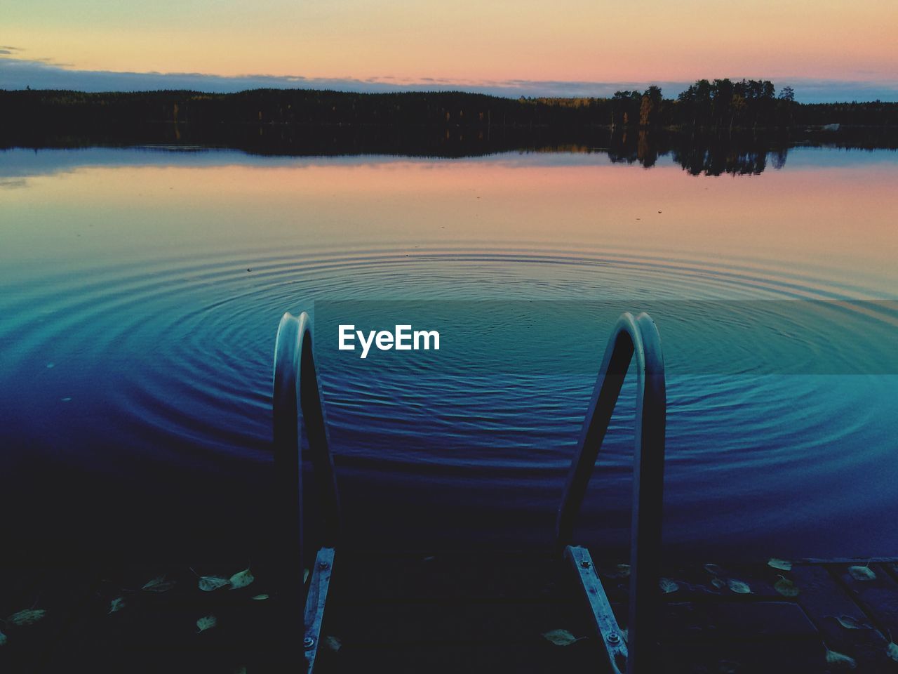 Railing by rippled lake during sunset