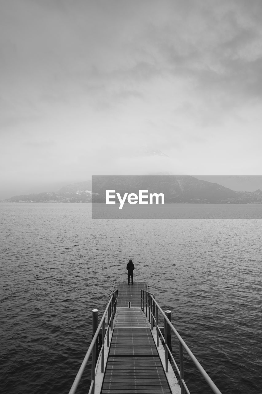 Rear view of man standing on jetty over lake against sky